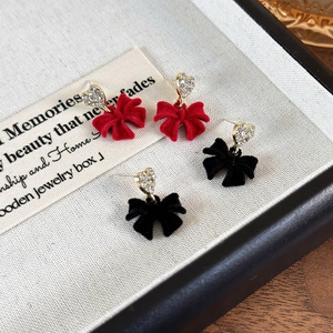 Macro detail of red and black velvet bow earrings with sparkling rhinestone hearts
