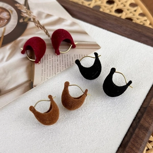 Macro shot of three pairs of velvet C-shaped hoop earrings in red, black, and dark brown