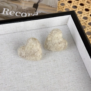 Nahaufnahme herzförmiger Ohrstecker aus Wollfilz mit weicher Textur in Beigebraun