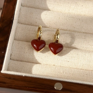 Close-up of heart-shaped red enamel drop earrings with gold hoops in a jewelry box