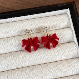 Close-up of red velvet bow earrings with heart-shaped rhinestone studs on white cloth