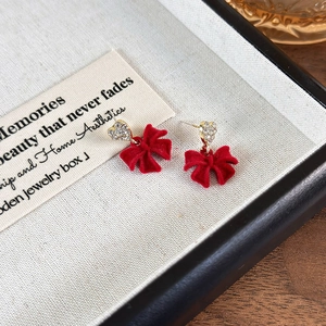 Close-up of red velvet bow earrings with rhinestone heart studs on a display tray