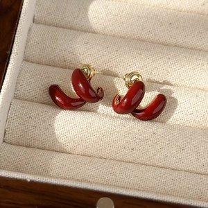 Detail of burgundy enamel C-shaped earrings with gold metal base on beige jewelry box