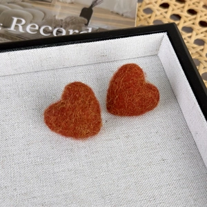 Nahaufnahme herzförmiger Ohrringe aus Wollfilz mit weicher Textur in Orange und Gelb