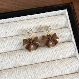 Macro detail of red velvet bow earrings with heart-shaped rhinestones on a jewelry tray