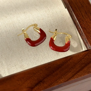 Detail of red enamel U-shaped hoop earrings with gold plating on textured linen fabric