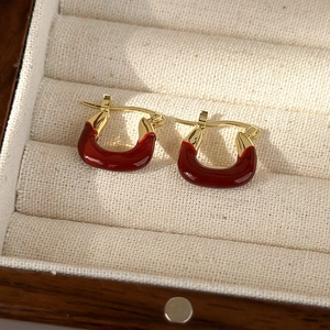 Close-up of vintage U-shaped earrings in red enamel and gold finish on fabric background
