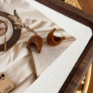 Close-up of elegant brown flocked C-shaped earrings with gold metal studs on a magazine
