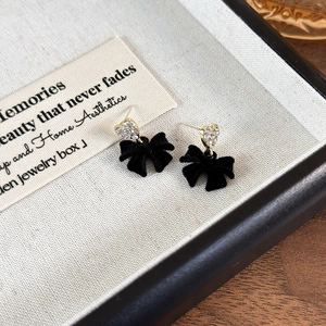 Macro shot of black velvet bow earrings with gold heart rhinestones on jewelry tray