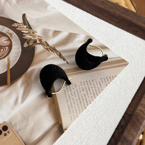 Detail view of C-shaped golden hoop earrings with black velvet texture on magazine page