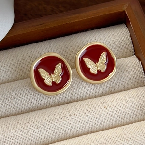 Detailed macro of red enamel butterfly stud earrings inside a beige jewelry gift box