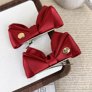 Détail de deux barrettes à nœuds en satin rouge foncé avec étiquettes métalliques