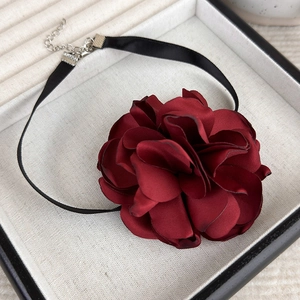 Detail of burgundy satin rose choker with black ribbon on a white jewelry tray