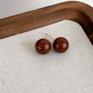 Primo piano di orecchini geometrici marroni con perni dorati su uno sfondo di tessuto di lino