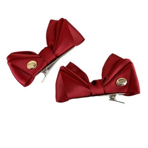 Paire de barrettes nœud en satin rouge avec charme métallique doré sur fond blanc