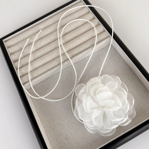 Détail d'un choker fleur de camélia blanc en relief sur un plateau de bijoux en velours
