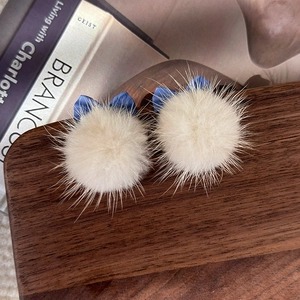 Gros plan de boucles d'oreilles en fourrure blanche avec nœuds bleus sur un plateau