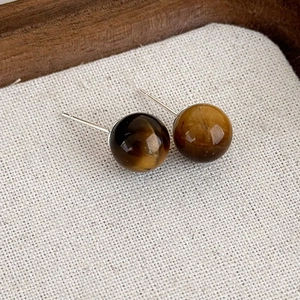 Macro dettagliata di orecchini vintage occhio di tigre su sfondo di tessuto crema strutturato