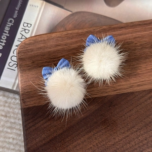 Détail des boucles d'oreilles avec nœud bleu et pompon blanc sur plateau en bois