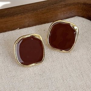 Dettaglio macro di orecchini geometrici dorati con smalto marrone in stile vintage