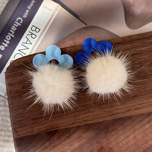 Gros plan de boucles d'oreilles en peluche d'hiver avec fleurs bleues sur un plateau en bois