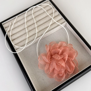 Détail d'une fleur de camélia en tissu rose pâle sur un collier choker à cordon blanc