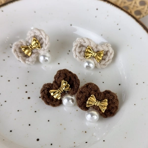 Detail of hand-knitted bow earrings with pearls in beige and brown colors on a ceramic tray