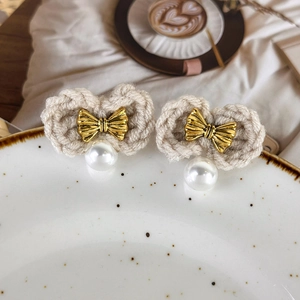 Close-up of knitted bow earrings with white pearls and gold accents on ceramic plate