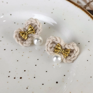 Detail of hand-knitted bow earrings with gold metal accents and white pearls