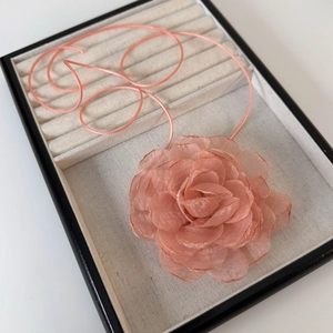 Vue détaillée du choker fleur de camélia en tissu rose corail sur plateau à bijoux