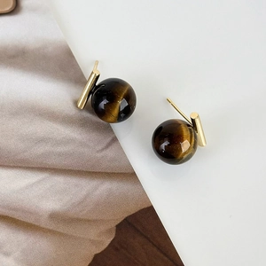 Macro view of spherical tiger eye stone earrings with golden bar detailing