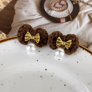 Close-up of caramel knitted earrings with gold bow and elegant pearl drop detail