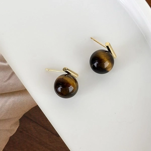 Close-up of golden tiger eye stud earrings with brown texture on a white tray