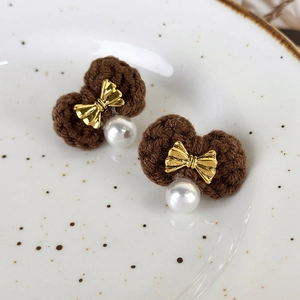 Macro shot of brown knitted bow earrings with gold metal accents and white pearls