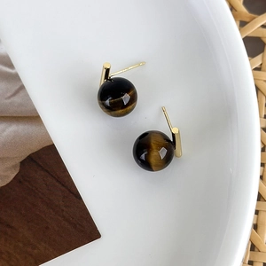 Detailed close-up of tiger eye stud earrings in a ceramic bowl with retro brown background
