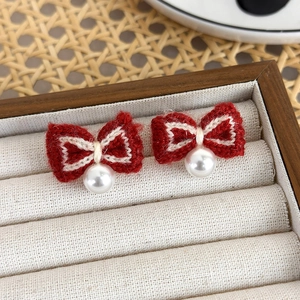 Detail of red knit bow earrings with white pearl pendants on a textured tray