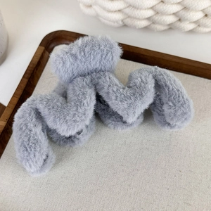 Vue détaillée d'une grande pince à cheveux grise en peluche ondulée sur un plateau en bois épuré
