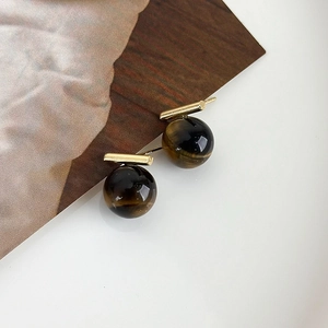 Macro detail of retro tiger eye stone earrings with golden bar on wooden prop
