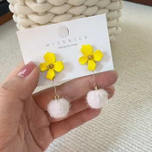 Detail of yellow flower earrings with white fur pom-poms on a display card