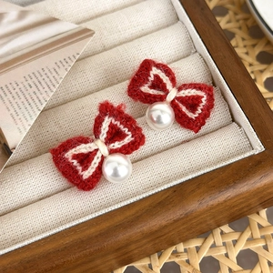 Macro detail of red knitted bow earrings with white pearl pendants in a wooden jewelry box