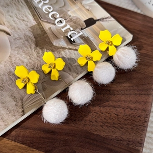 Chic yellow flower earrings with white faux fur pom poms on a rustic wooden table