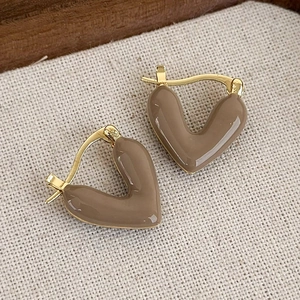 Dettaglio di orecchini a cuore in smalto marrone caffè su tessuto beige minimalista