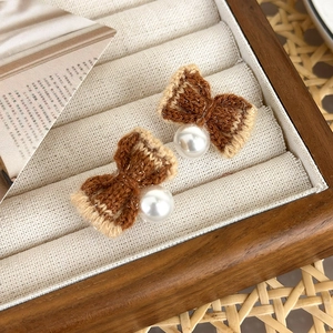 Detailed close-up of knitted bow earrings with central pearl on a soft velvet display