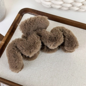 Détail d'une grande pince à cheveux en peluche marron foncé sur un plateau en lin élégant