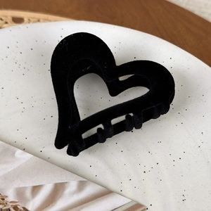 Macro shot of black flocked heart hair claw clip with velvet texture on ceramic tray