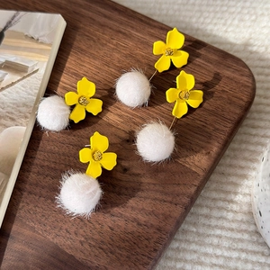 Detail of yellow flower earrings with white fur balls on a dark wooden display tray
