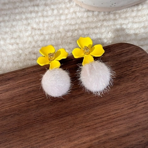 Detailed shot of yellow metal flower earrings with soft pink fluffy pom pom drops