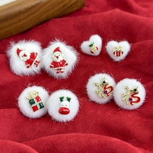 Detailed close-up of plush white pompom earrings with festive Christmas charms on red fabric