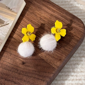 Detailed view of yellow 3D flower earrings with white faux fur pom poms on dark wood