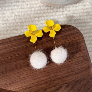 Detail of yellow flower earrings with white pompom pendant on textured background